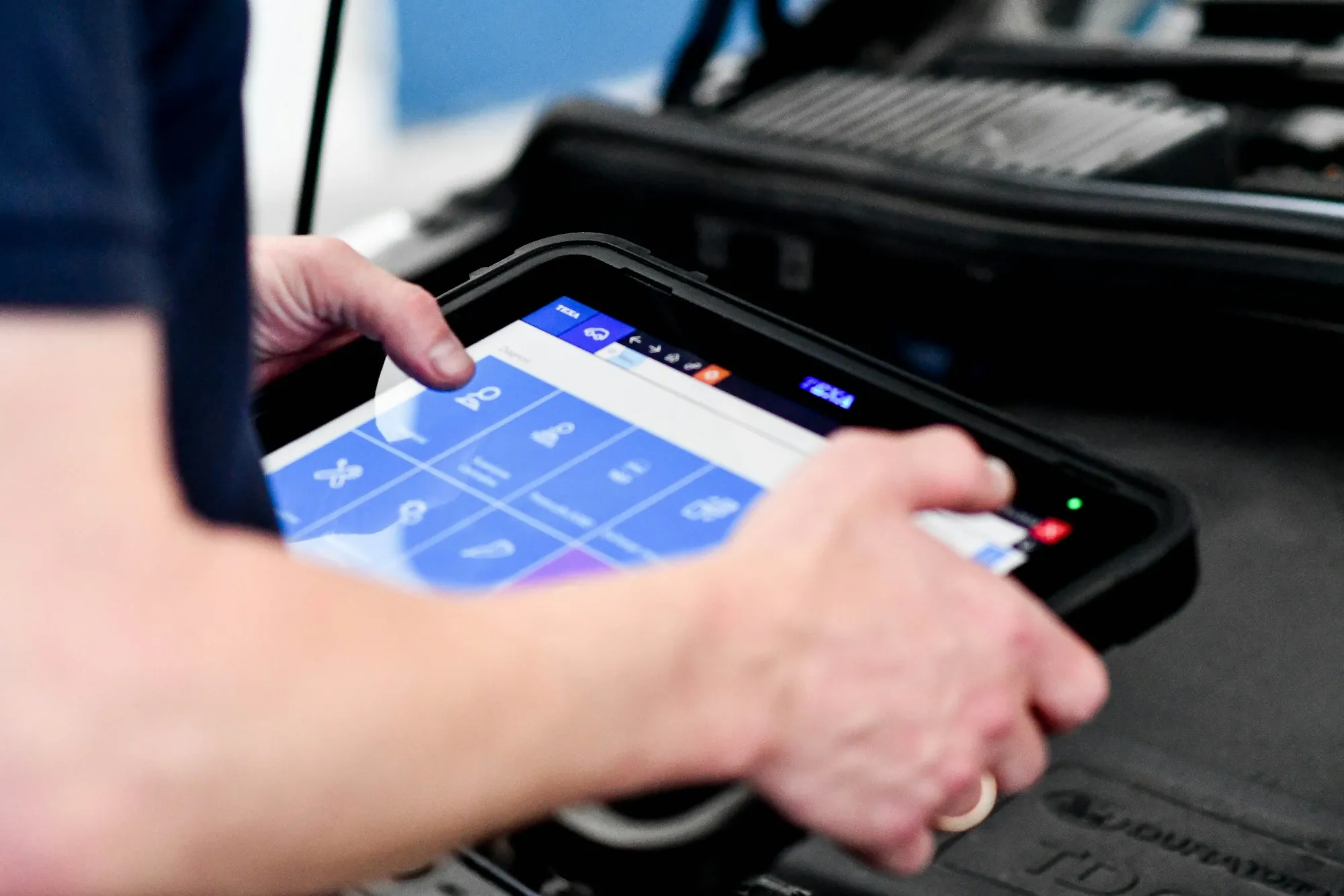 Hand holding a diagnostic tablet connected to a vehicle