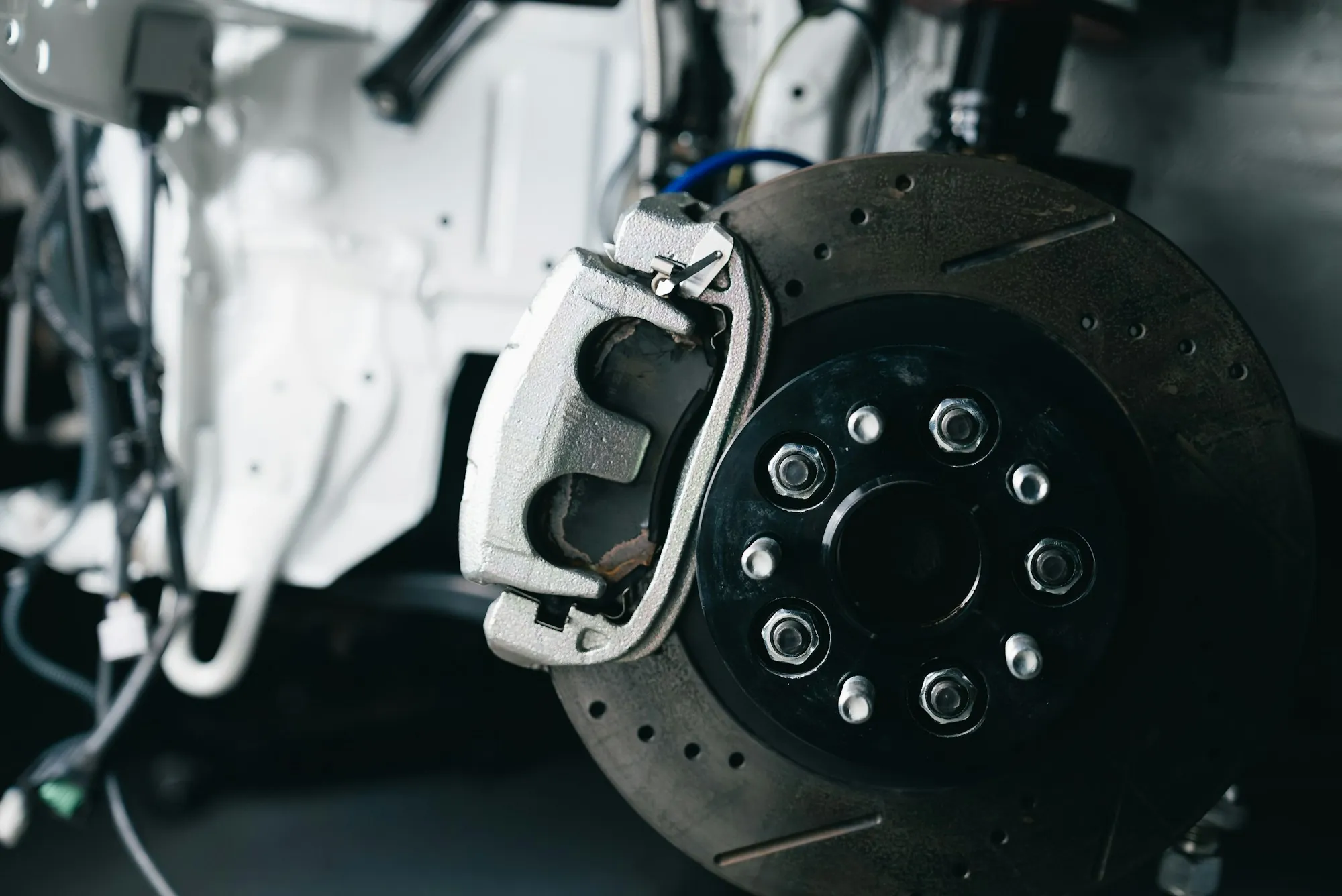 Cross-drilled brake rotor and caliper on a vehicle in the shop
