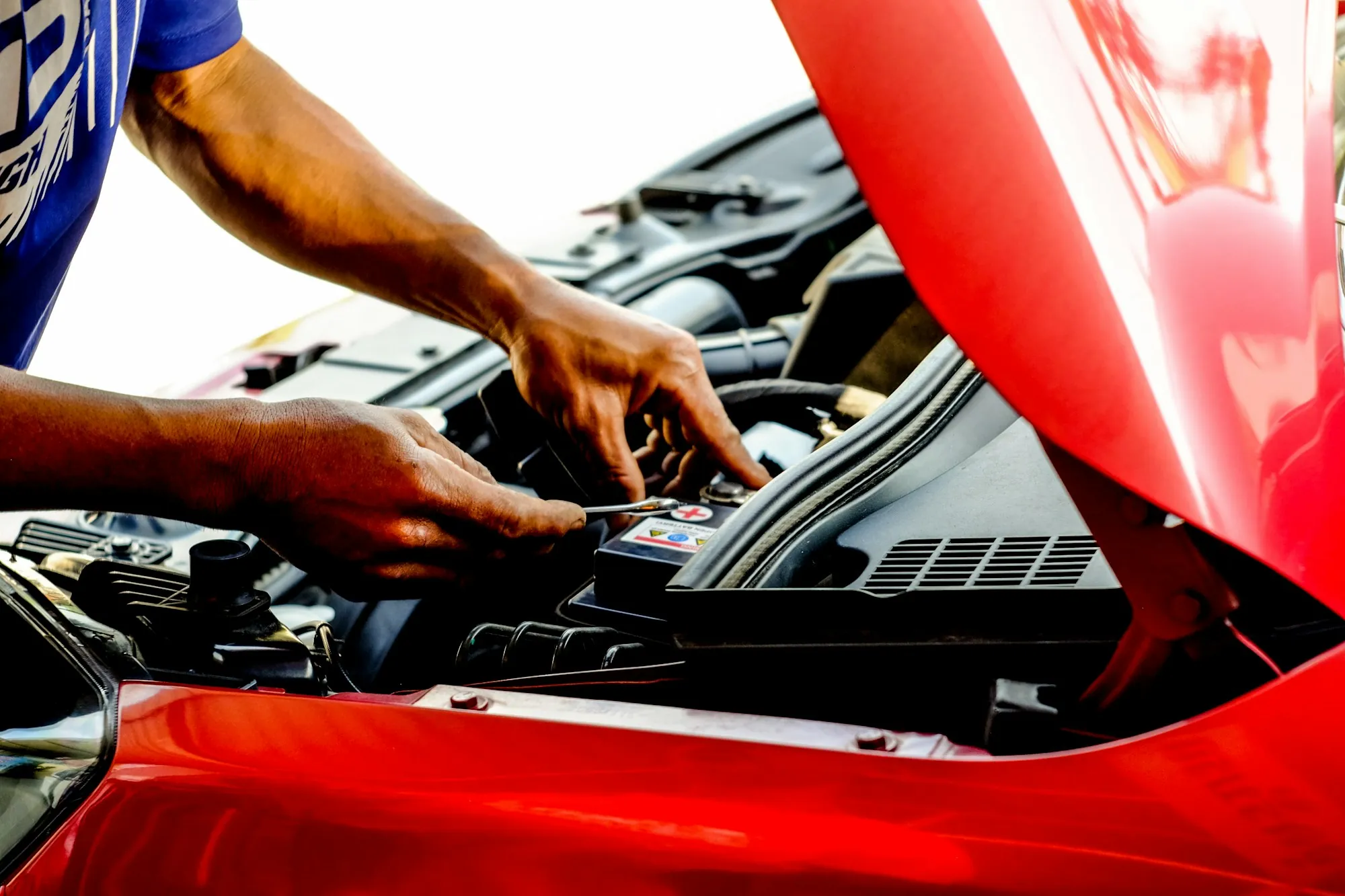 Hands working in the engine bay of a red car