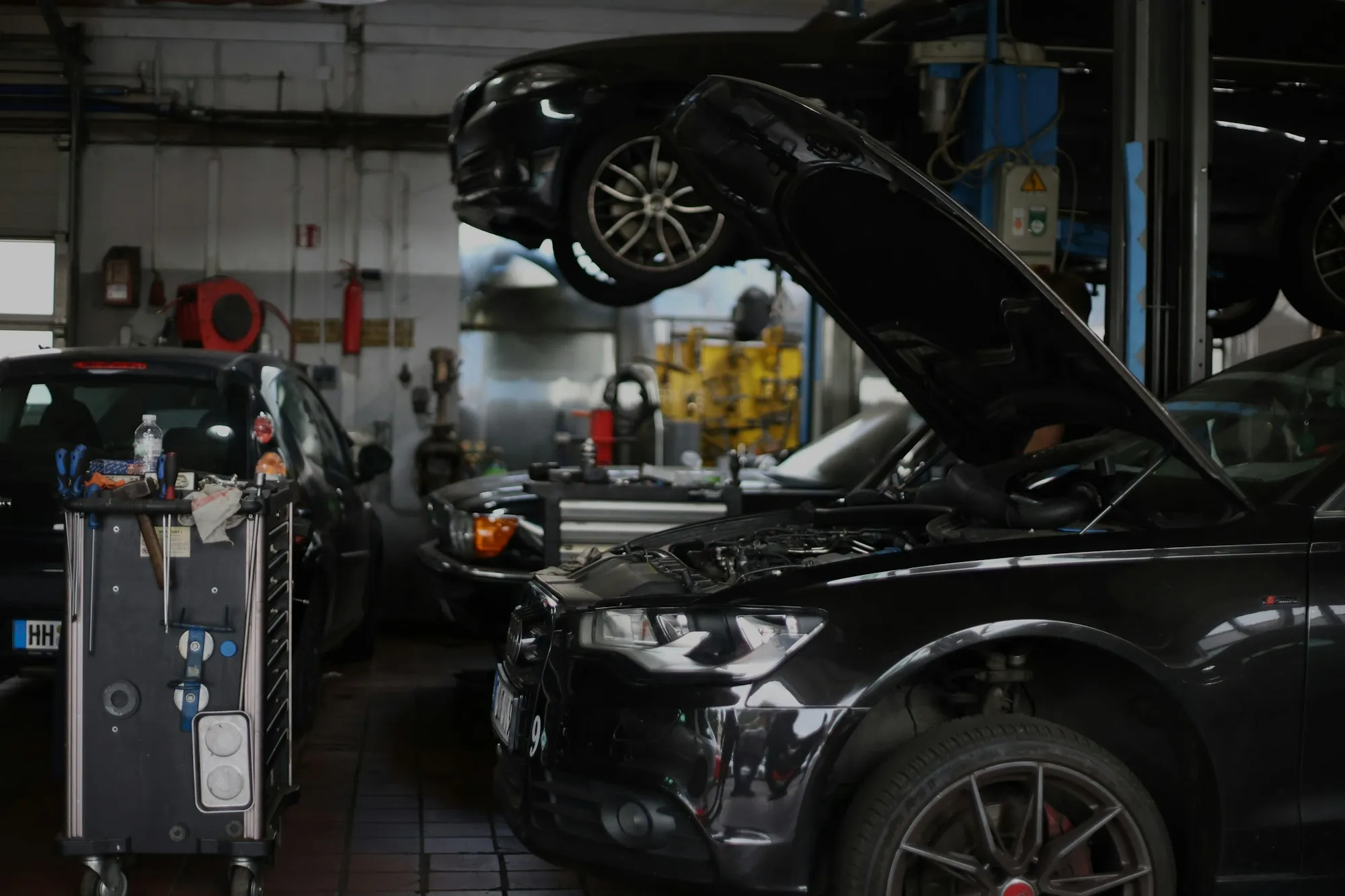 Technician working under the open hood of a dark SUV in a repair bay