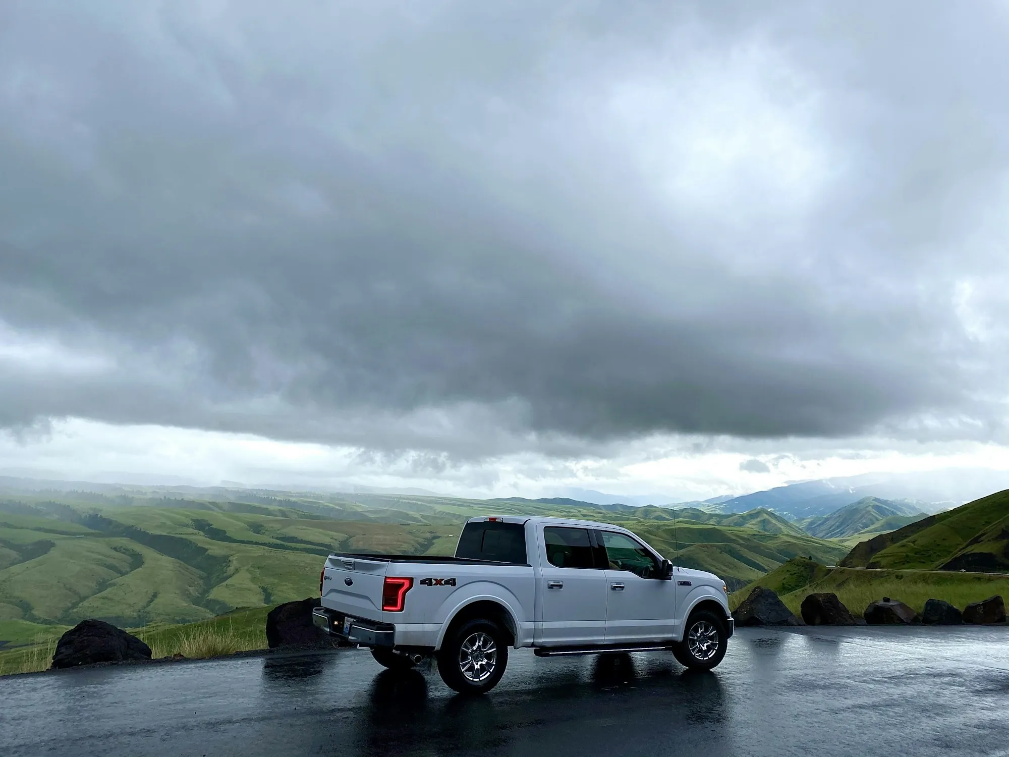 White pickup truck parked on a wet road with green hills and storm clouds